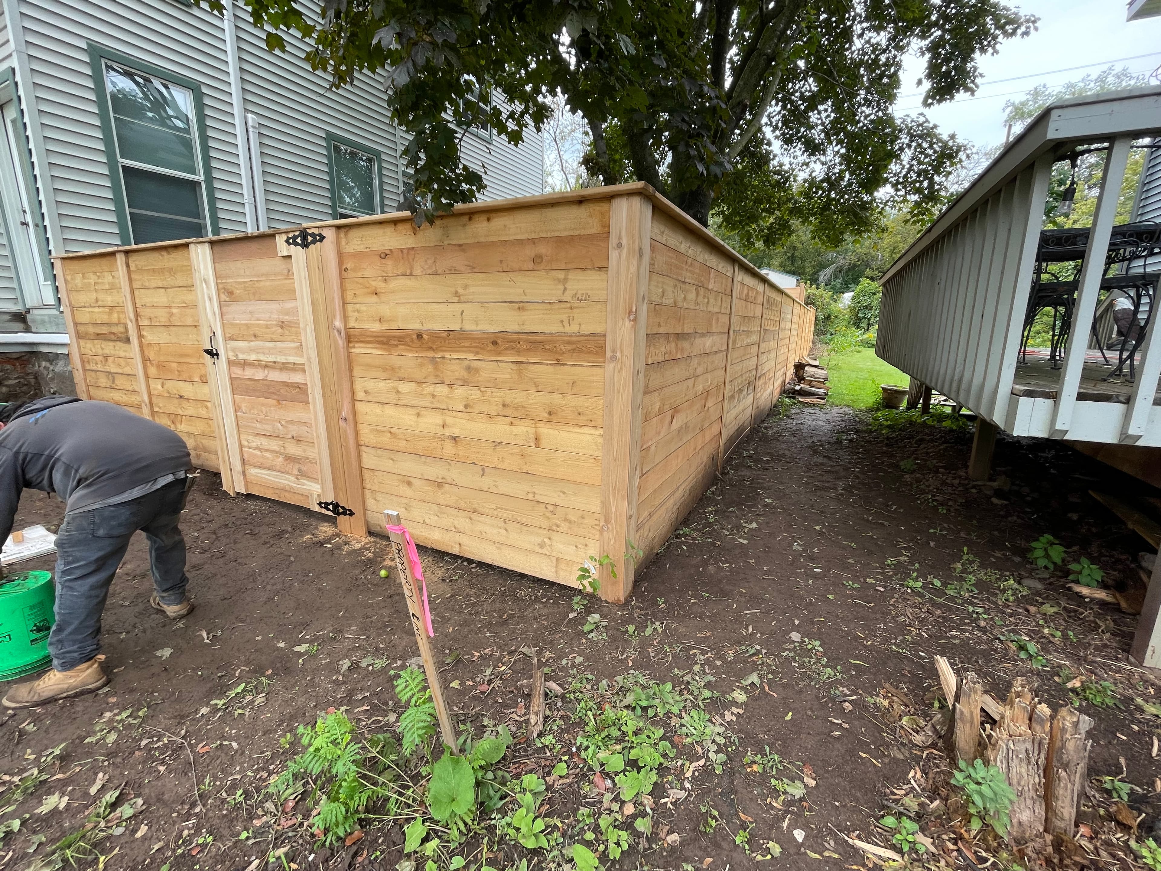 Newly installed horizontal wooden privacy fence with a gate in a residential dirt backyard.