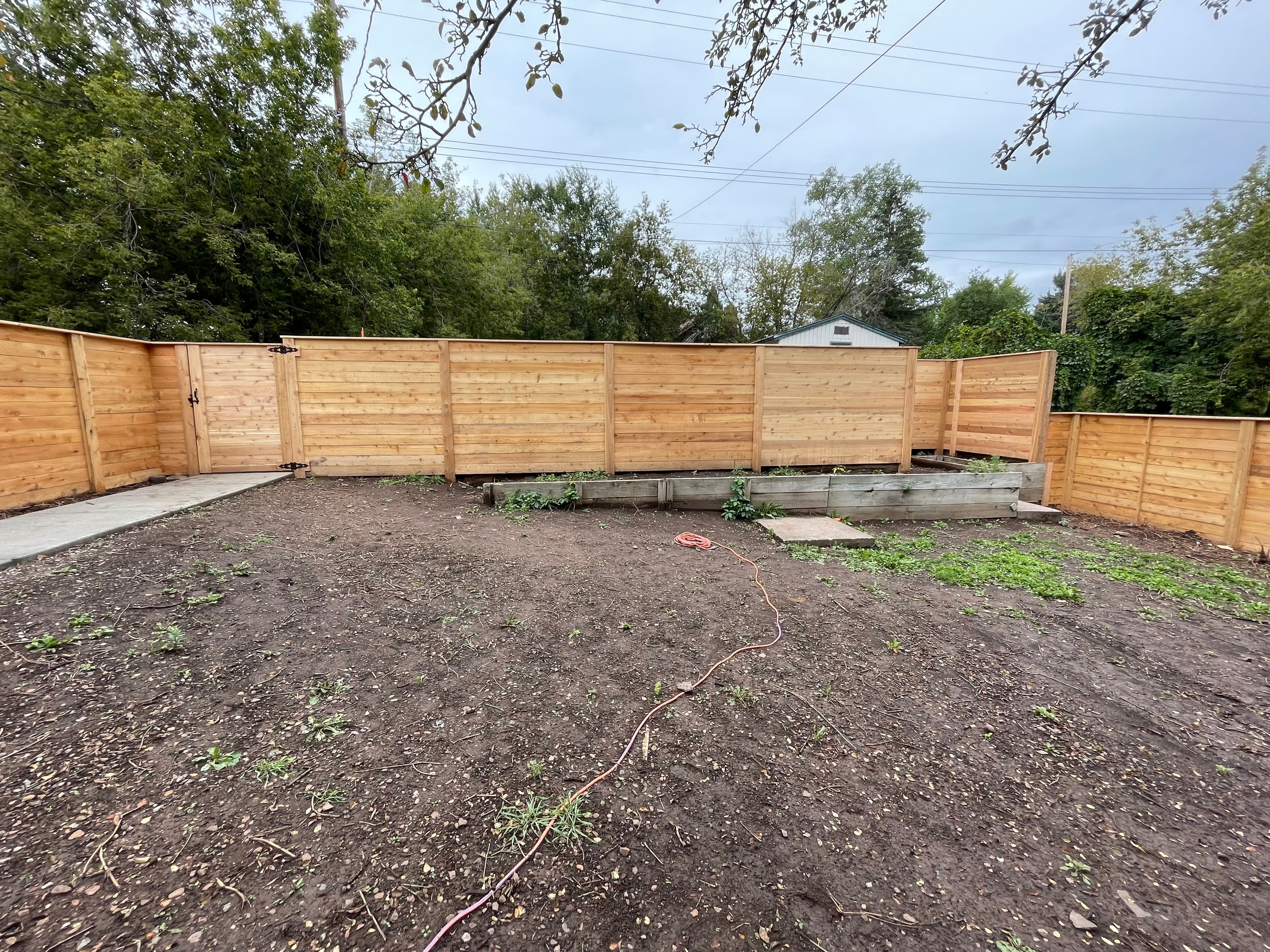 Horizontal wooden fence in a backyard with bare dirt ground and a raised garden bed.