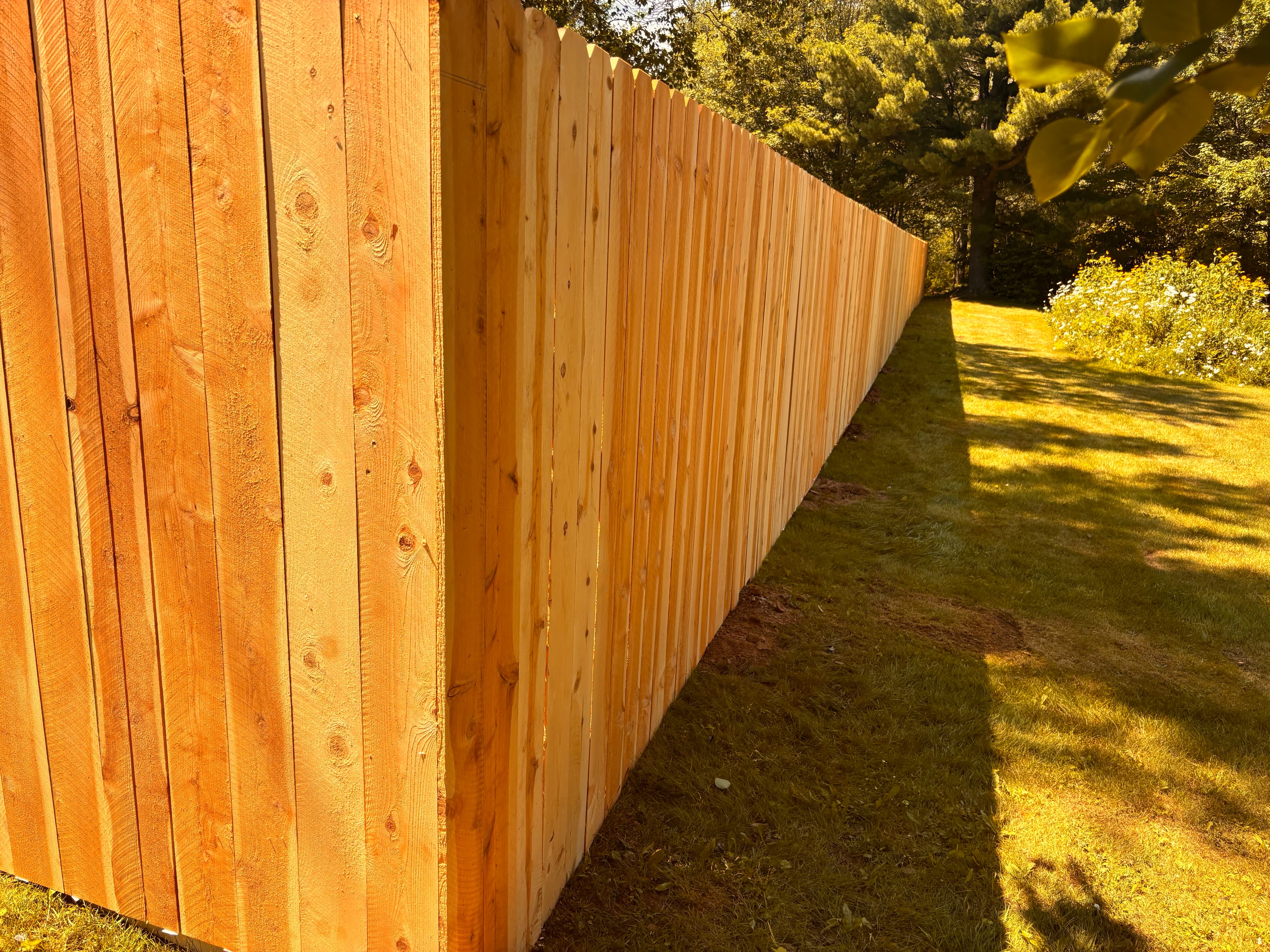 Perspective view of vertical wooden fence planks receding into the distance across a sunlit lawn.